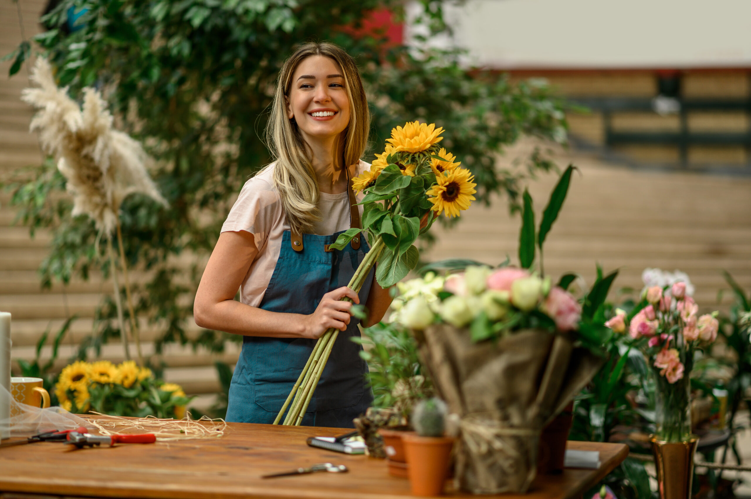 Beautiful woman florist standing and holding bouquet of sunflowers in flower shop
